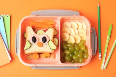 Photo of Lunch box with snacks and stationery on orange background, flat lay