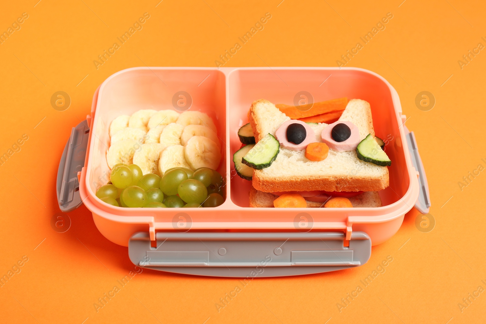 Photo of Lunch box with sandwich and fruits on orange background