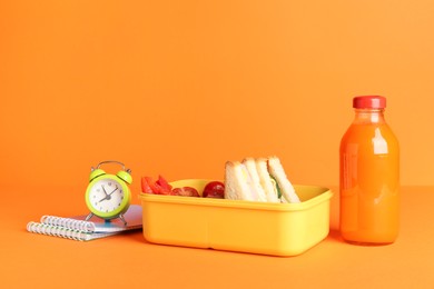 Photo of Lunch box with snacks, bottle of juice, alarm clock and notebooks on orange background