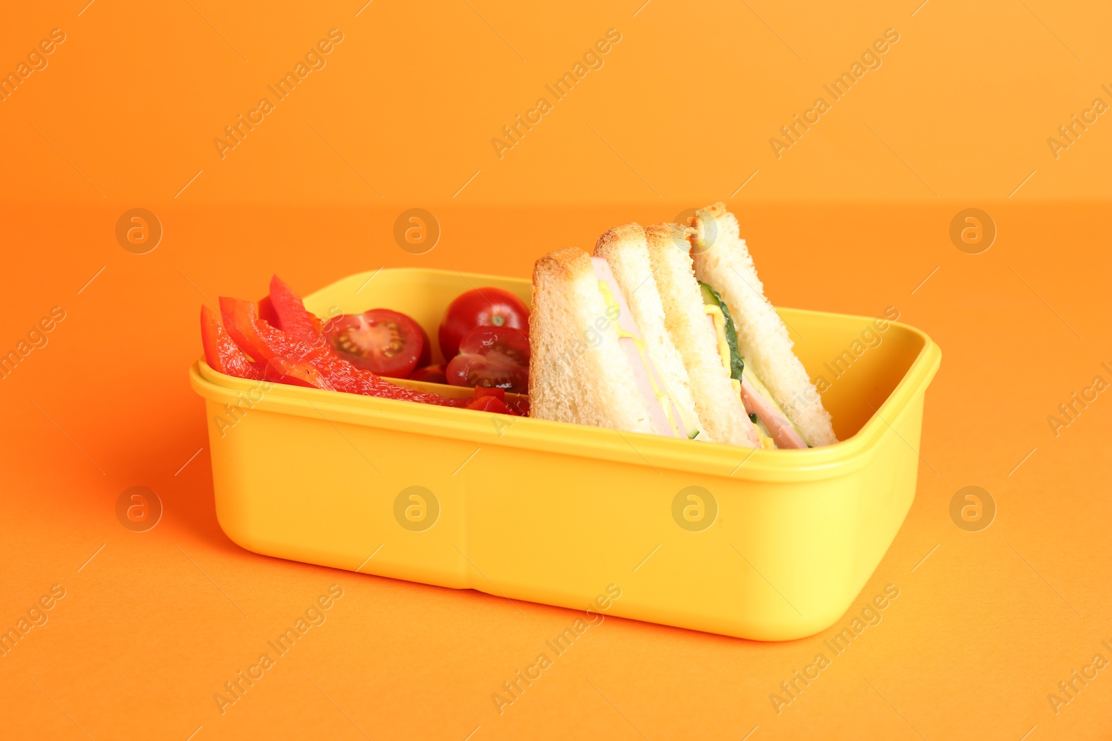 Photo of Lunch box with sandwiches and vegetables on orange background