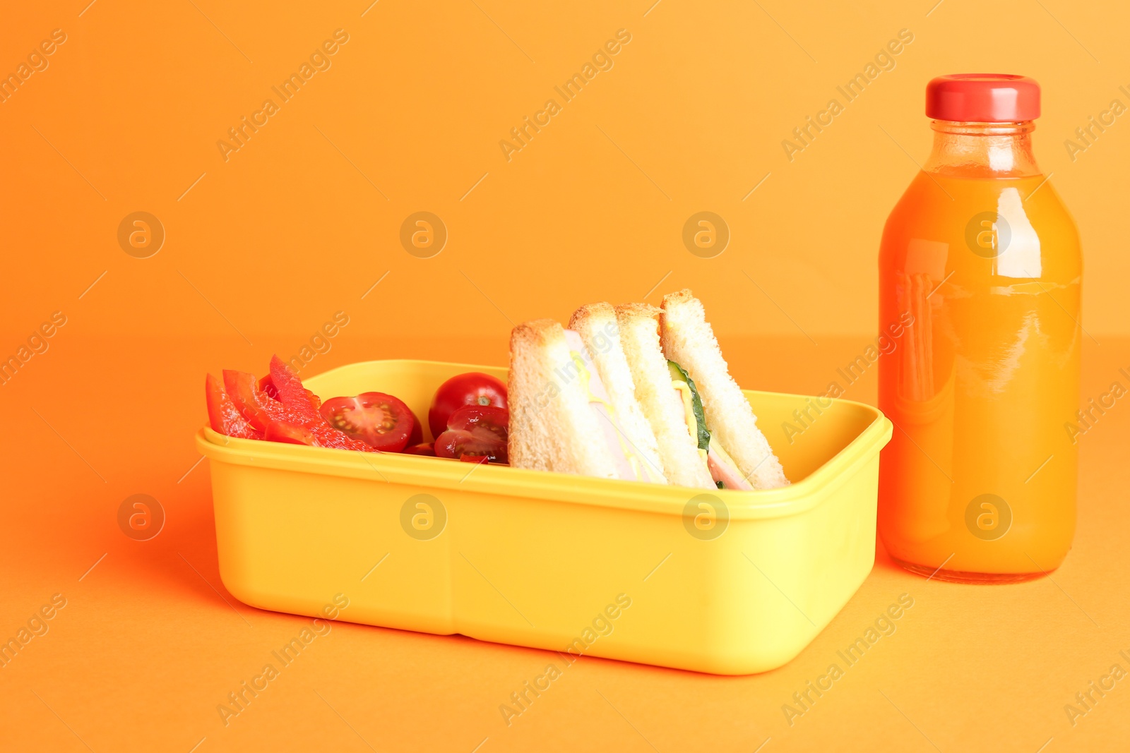 Photo of Lunch box with snacks and bottle of juice on orange background