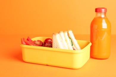 Photo of Lunch box with snacks and bottle of juice on orange background