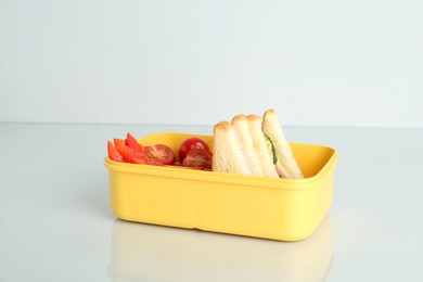 Photo of Lunch box with sandwiches and vegetables on light background