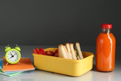 Photo of Lunch box with snacks, bottle of juice, alarm clock and stationery on light table