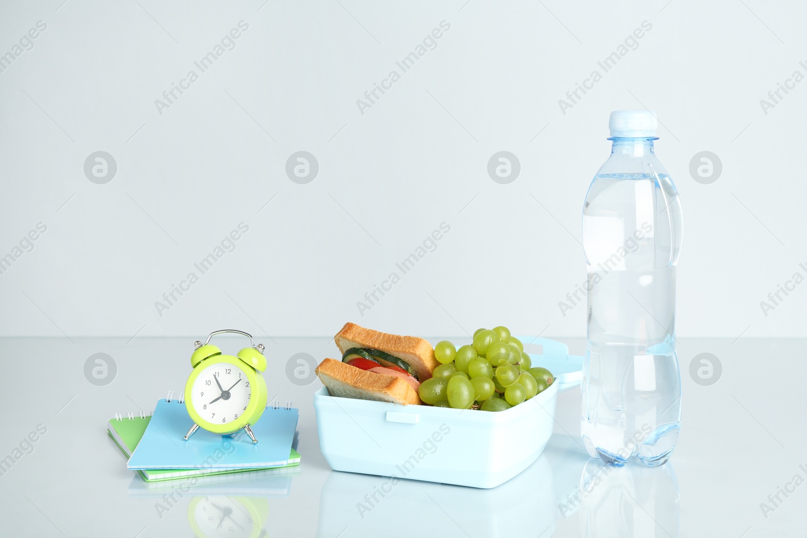 Photo of Lunch box with snacks, bottle of water, alarm clock and stationery on white background