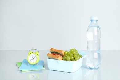 Photo of Lunch box with snacks, bottle of water, alarm clock and stationery on white background