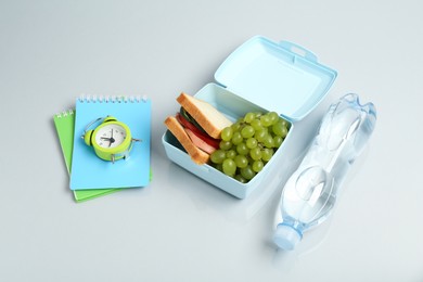 Photo of Lunch box with snacks, bottle of water, alarm clock and stationery on white table