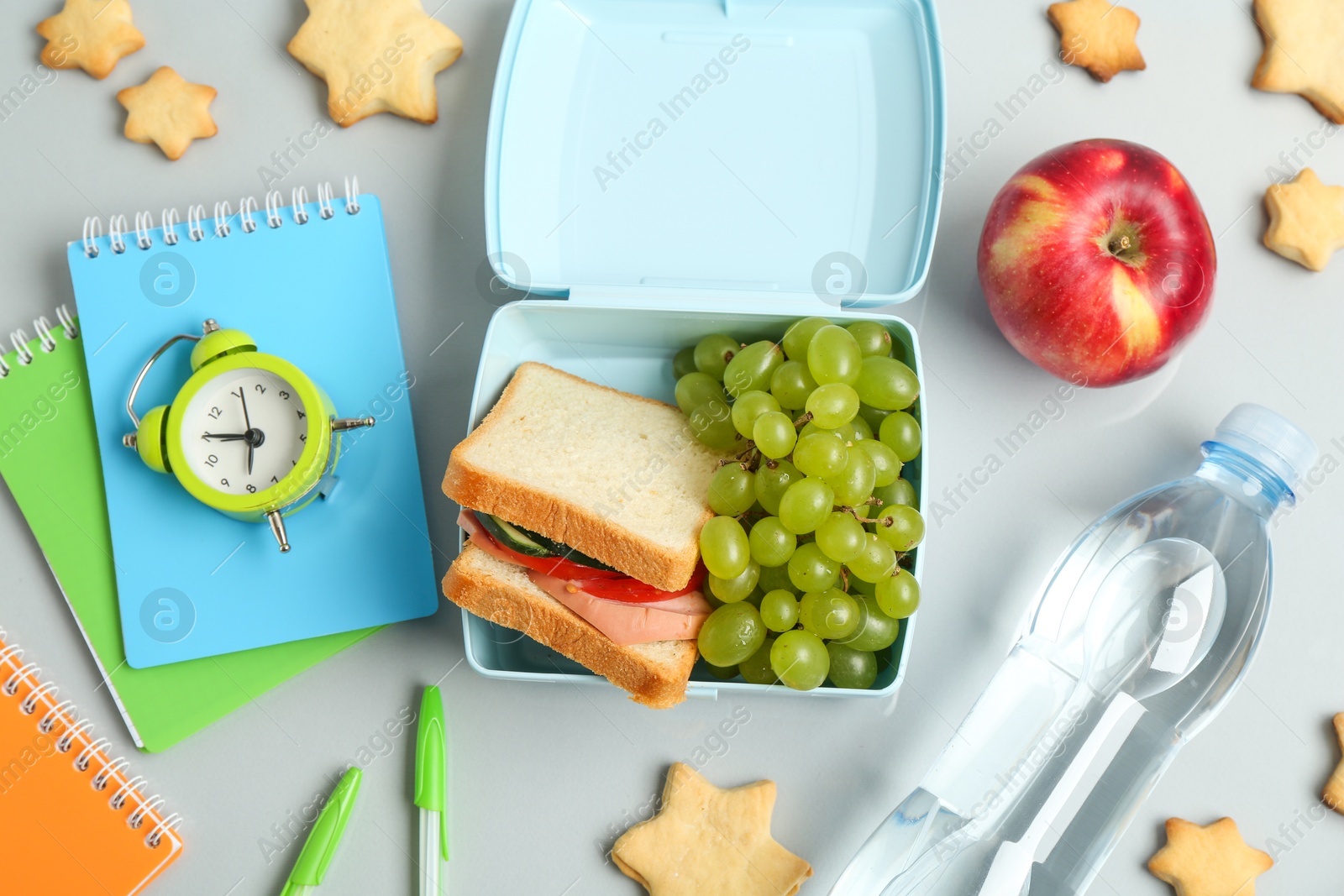 Photo of Lunch box with snacks, bottle of water, alarm clock and stationery on white background, flat lay