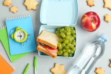 Photo of Lunch box with snacks, bottle of water, alarm clock and stationery on white background, flat lay