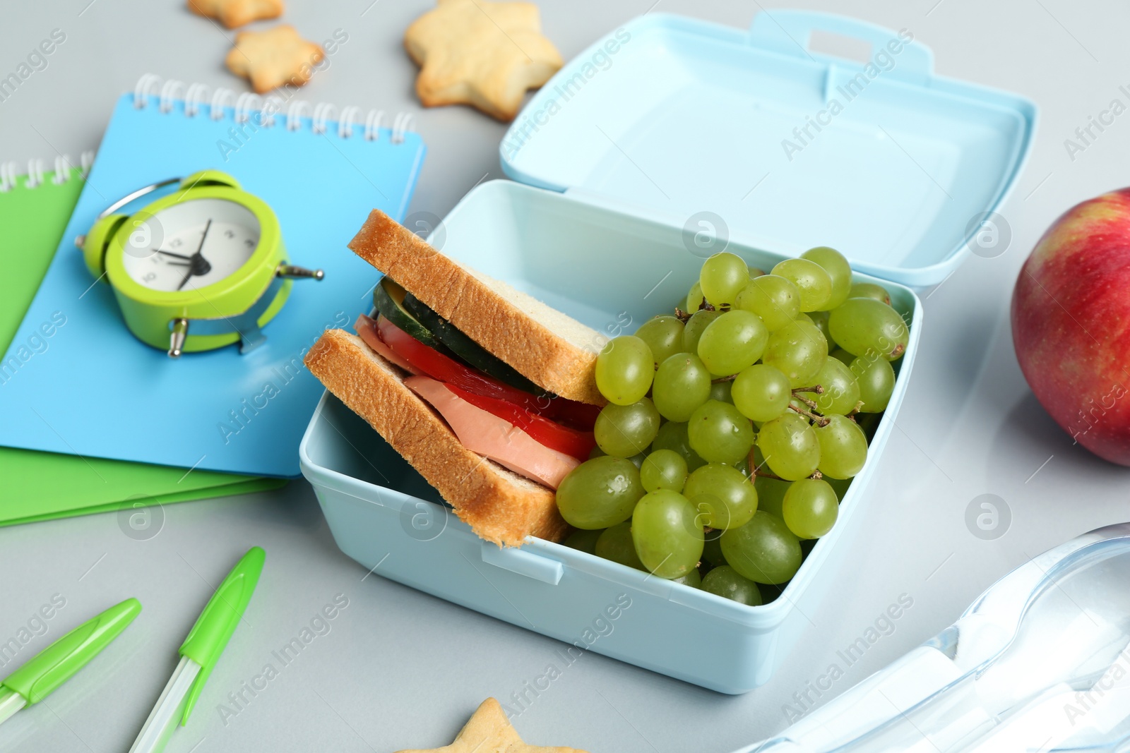 Photo of Lunch box with snacks, bottle of water, alarm clock and stationery on white table