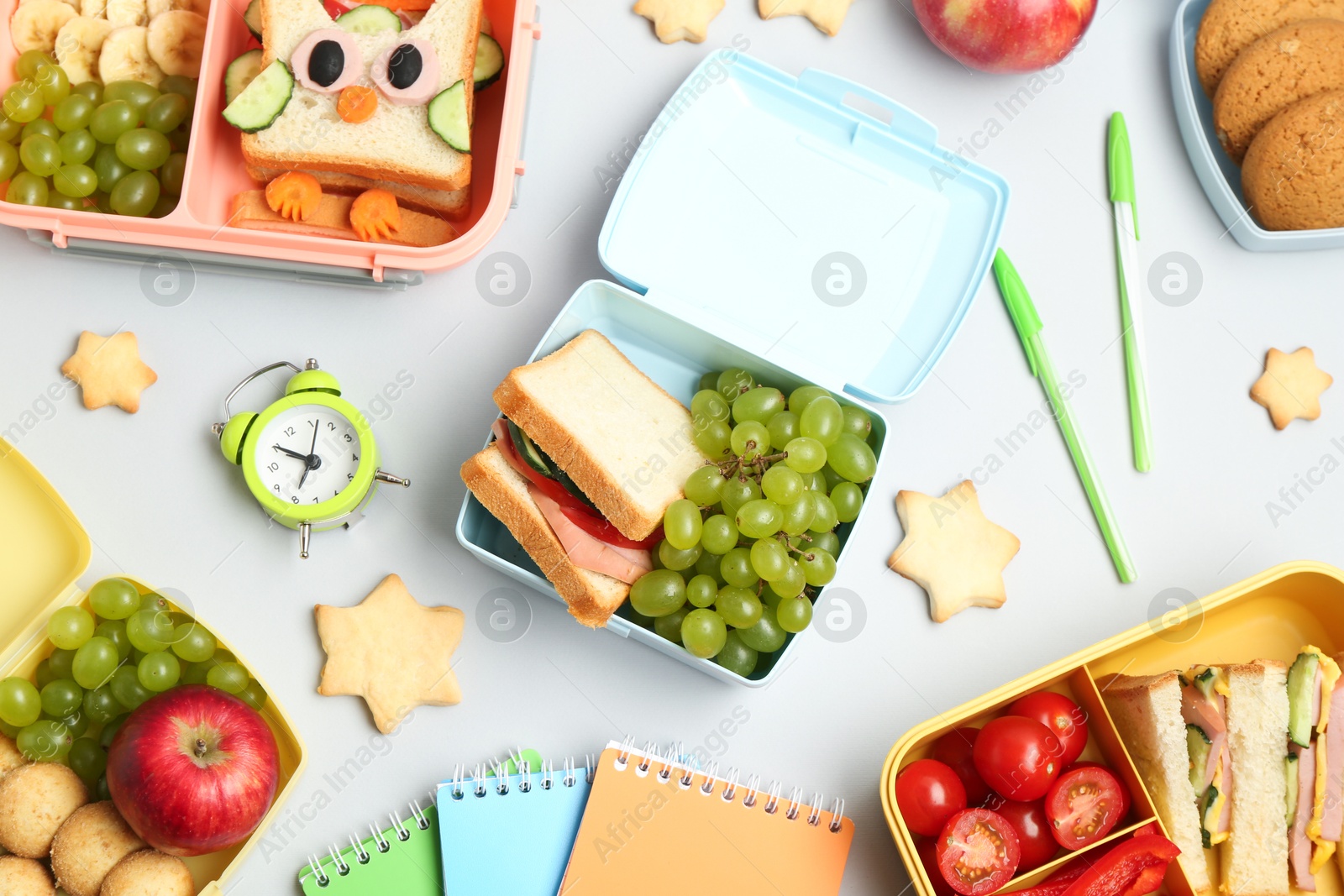 Photo of Lunch box with snacks, alarm clock and stationery on white background, flat lay