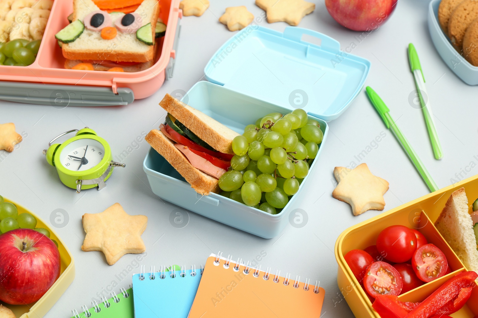 Photo of Lunch box with snacks, alarm clock and stationery on white table