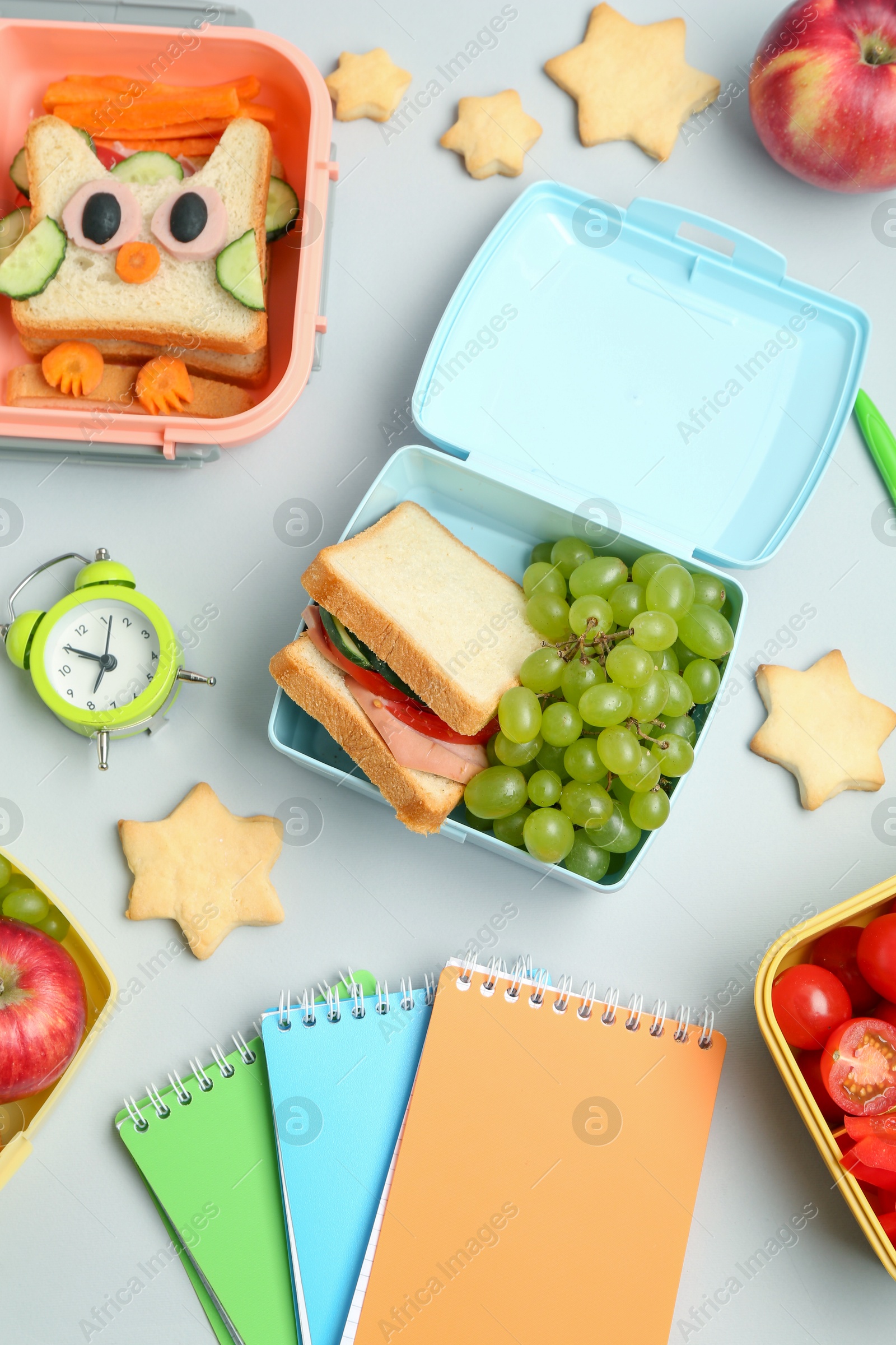 Photo of Lunch box with snacks, alarm clock and stationery on white background, flat lay