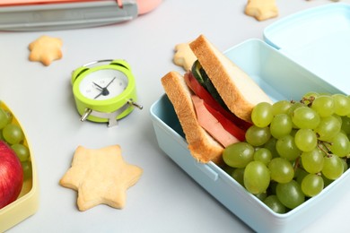 Photo of Lunch box with snacks, alarm clock and stationery on white table