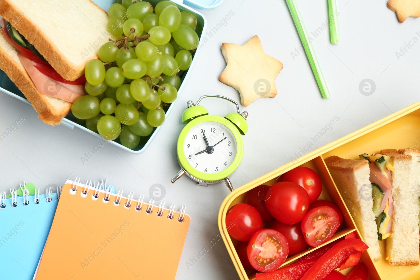 Photo of Lunch box with snacks, alarm clock and stationery on white background, flat lay