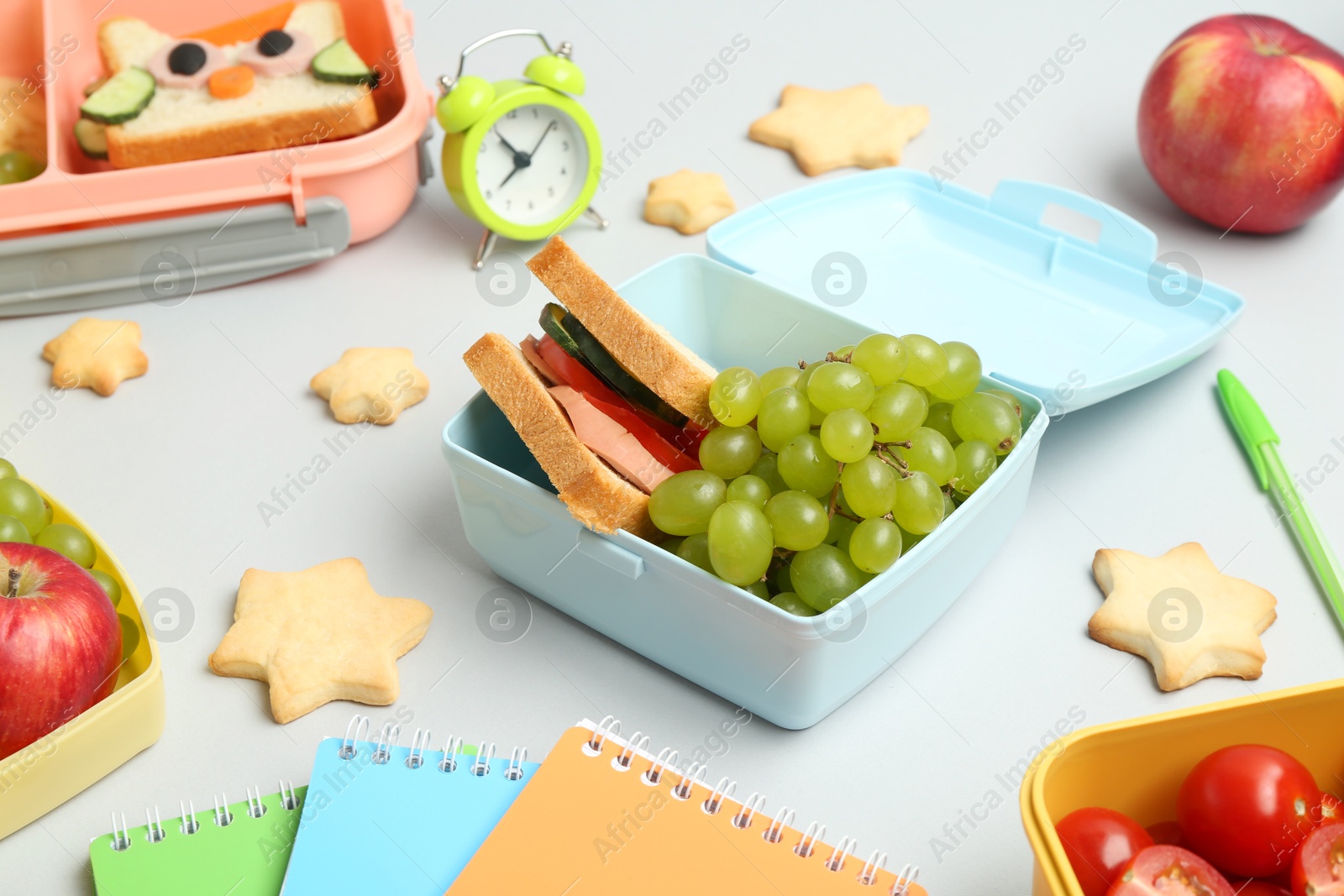 Photo of Lunch box with snacks, alarm clock and stationery on white table