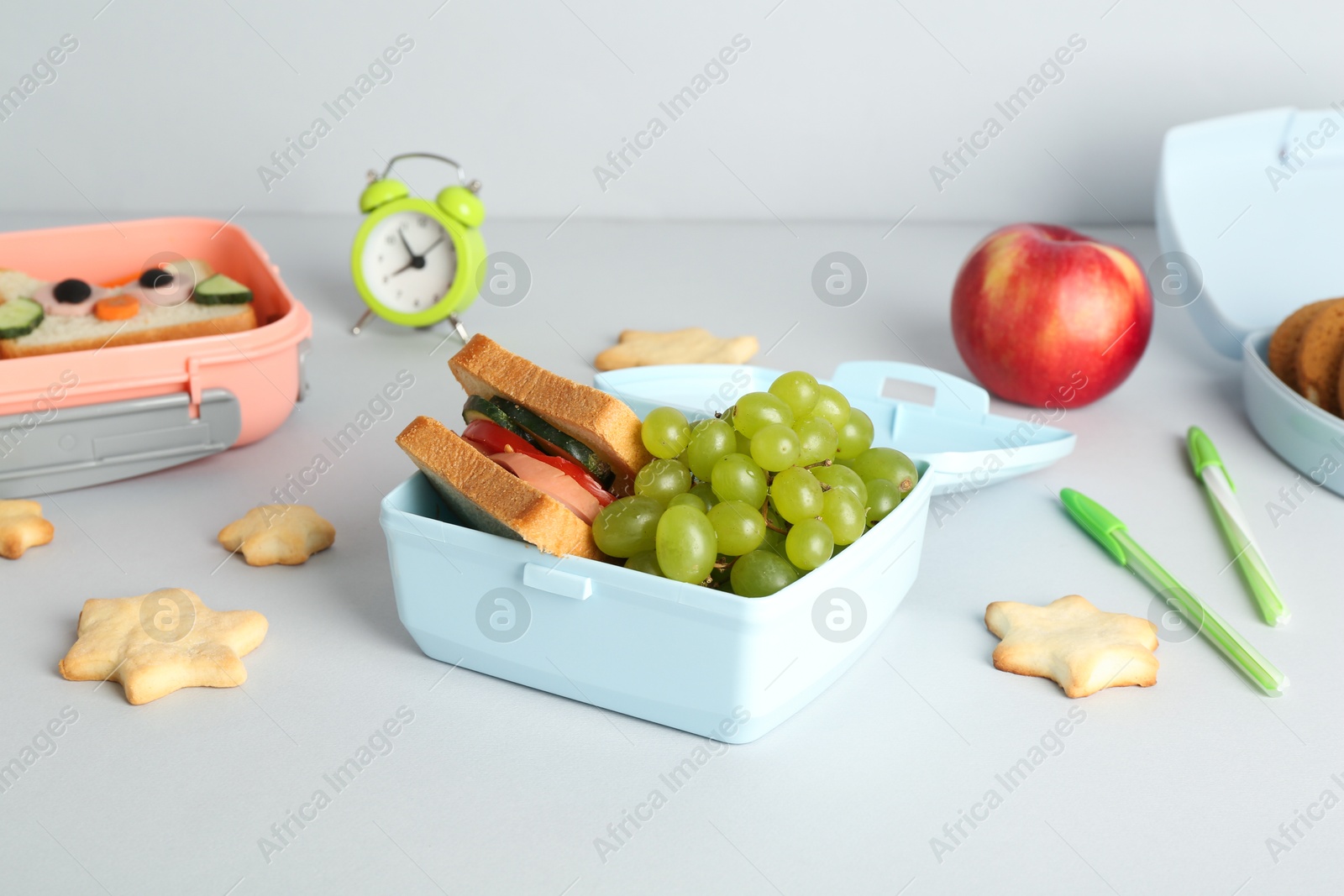 Photo of Lunch box with snacks, alarm clock and stationery on white table