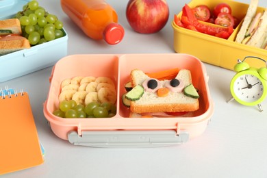 Photo of Lunch boxes with snacks, bottle of juice, alarm clock and stationery on white table