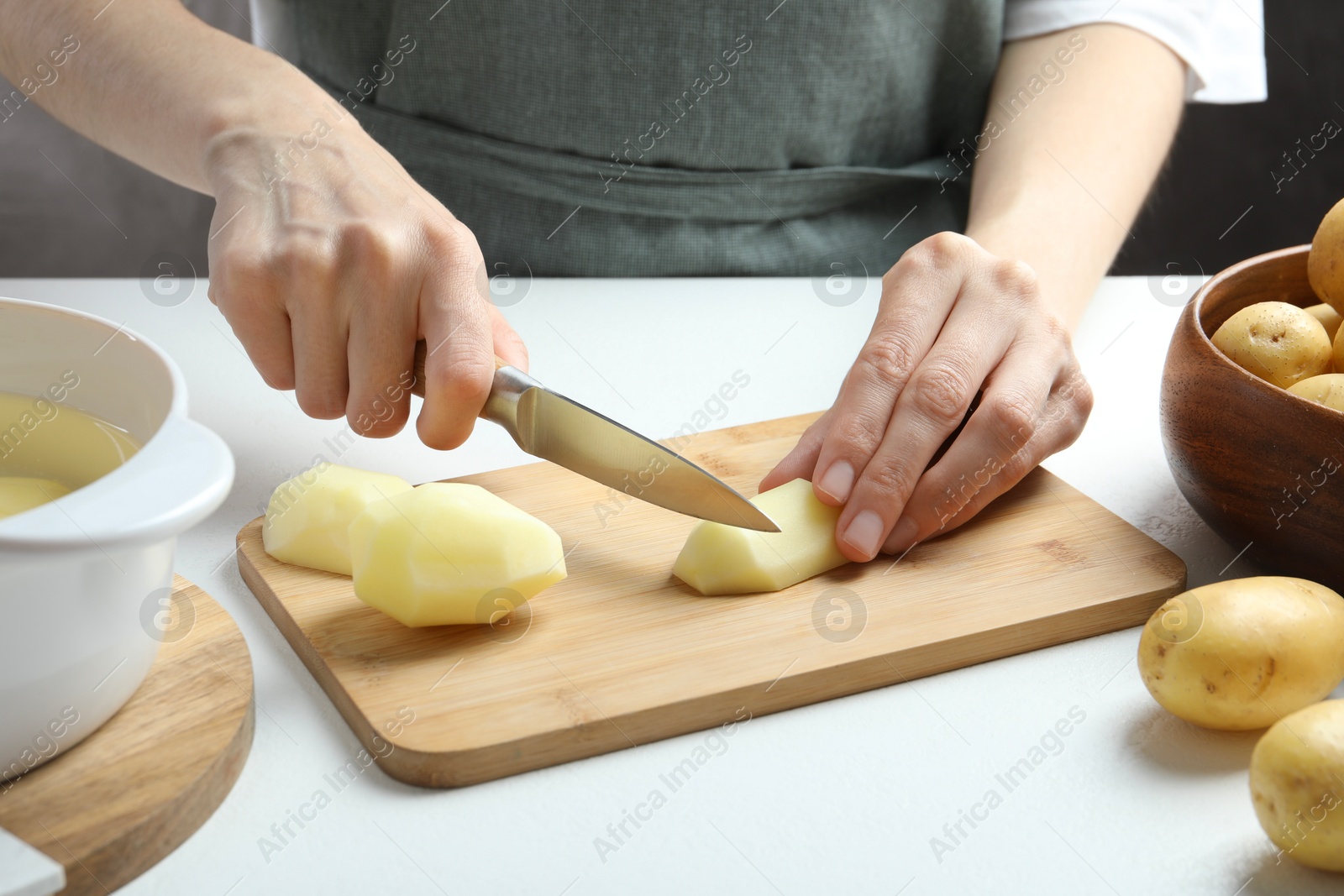 Photo of Woman cutting raw potato at white table, closeup