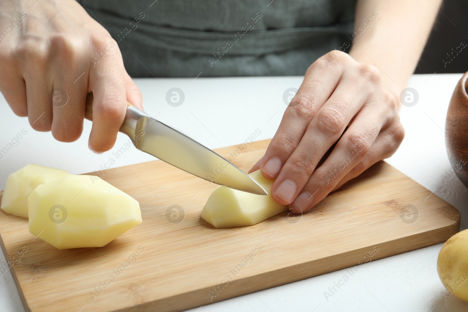 Photo of Woman cutting raw potato at white table, closeup