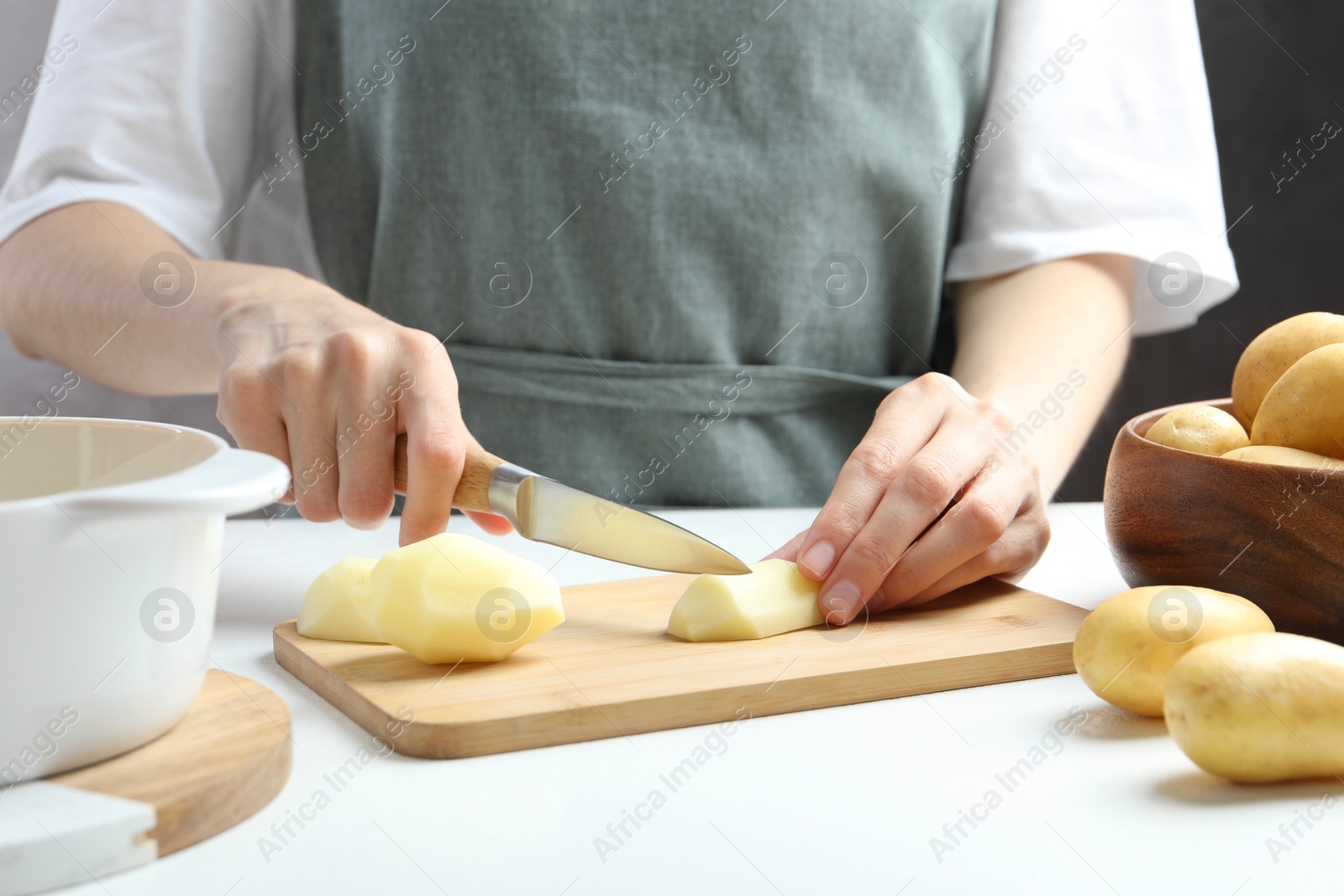 Photo of Woman cutting raw potato at white table, closeup