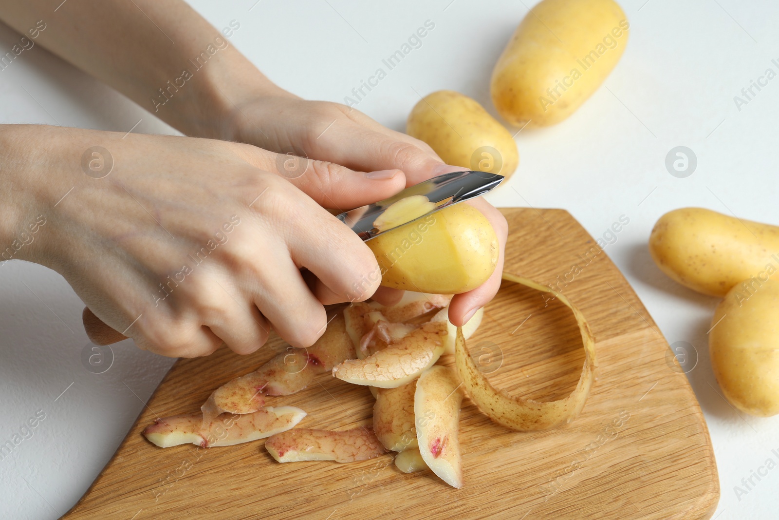 Photo of Woman peeling fresh potato with peeler at white table, closeup