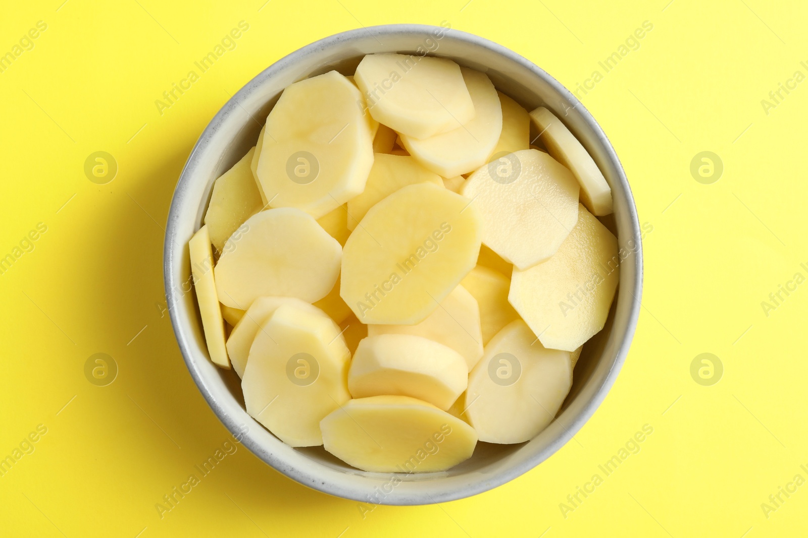 Photo of Cut fresh raw potatoes in bowl on yellow background, top view