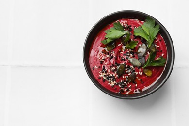 Photo of Tasty beetroot hummus, parsley and sesame in bowl on white table, top view. Space for text