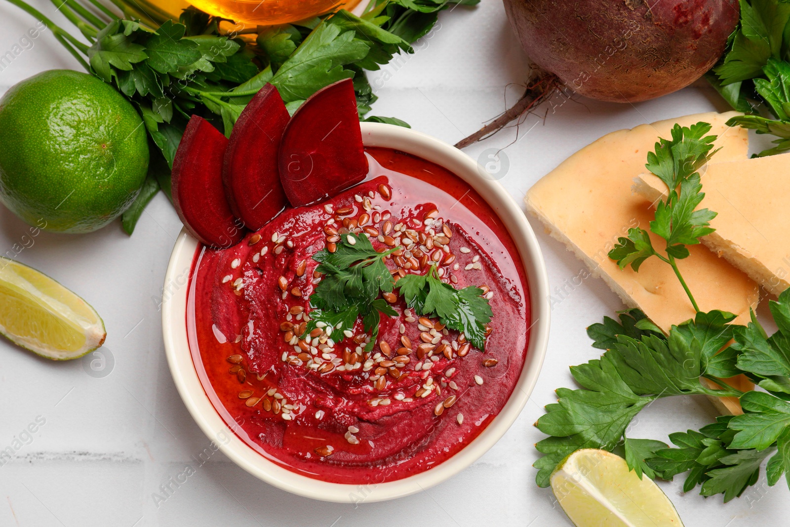 Photo of Tasty beetroot hummus in bowl and products on white table, flat lay