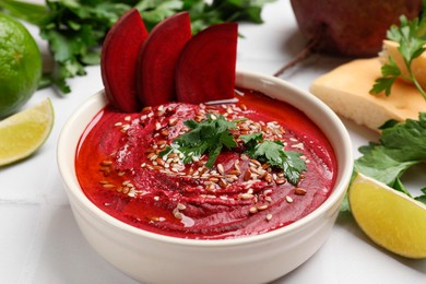 Photo of Tasty beetroot hummus in bowl and products on white table, closeup