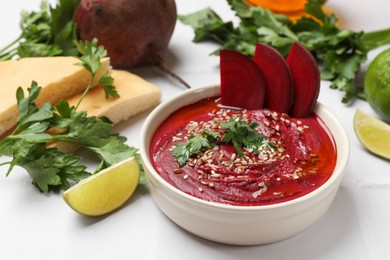 Photo of Tasty beetroot hummus in bowl and products on white table