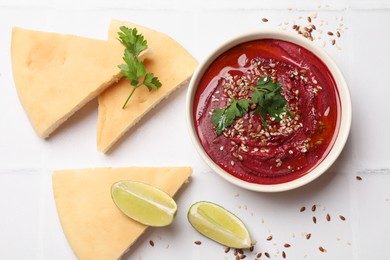 Photo of Tasty beetroot hummus in bowl and products on white table, flat lay