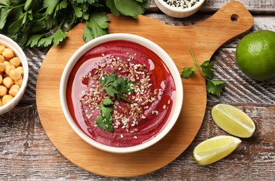 Photo of Tasty beetroot hummus in bowl and products on wooden table, flat lay