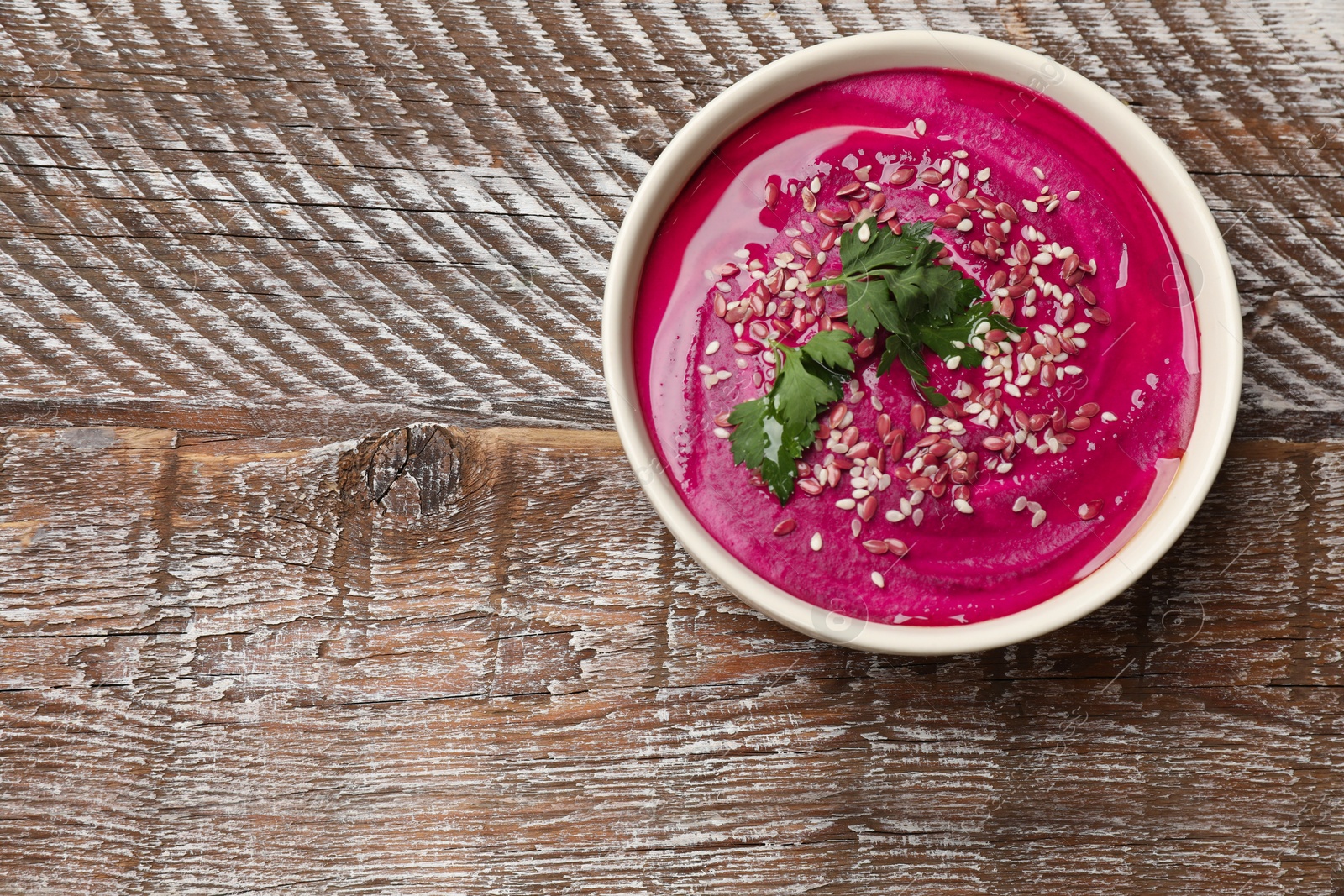 Photo of Tasty beetroot hummus, parsley and seeds in bowl on wooden table, top view. Space for text