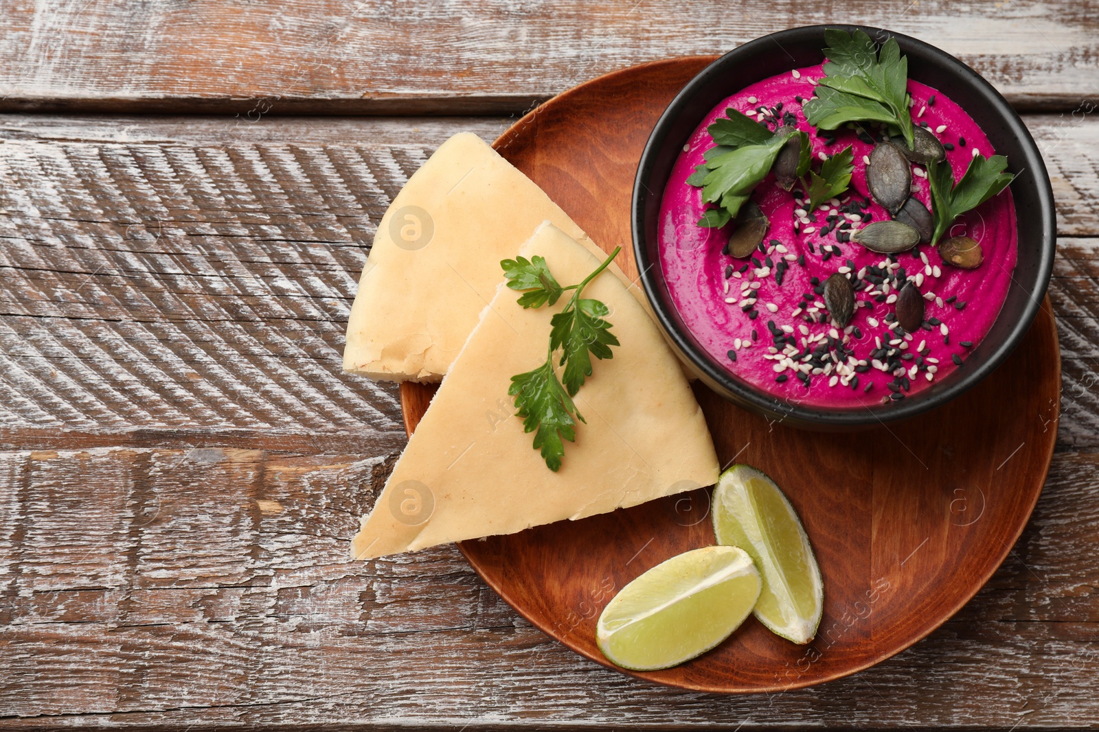 Photo of Tasty beetroot hummus in bowl and products on wooden table, top view. Space for text