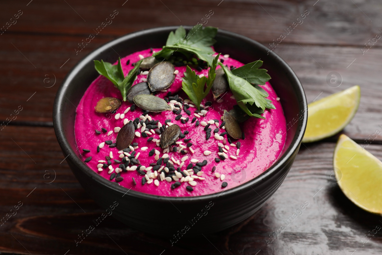 Photo of Tasty beetroot hummus, parsley and seeds in bowl on wooden table, closeup