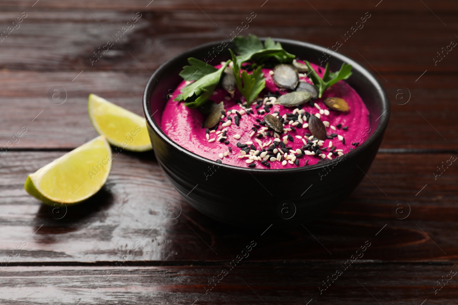 Photo of Tasty beetroot hummus, parsley and seeds in bowl on wooden table, closeup