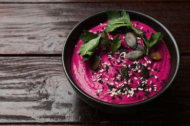 Photo of Tasty beetroot hummus, parsley and seeds in bowl on wooden table, closeup. Space for text