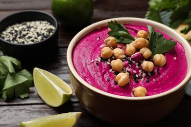 Photo of Tasty beetroot hummus in bowl and products on wooden table, closeup