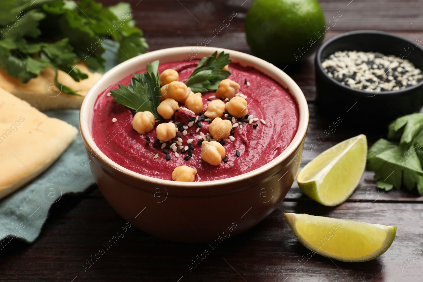 Photo of Tasty beetroot hummus in bowl and products on wooden table, closeup