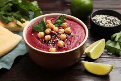 Photo of Tasty beetroot hummus in bowl and products on wooden table, closeup