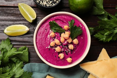 Tasty beetroot hummus in bowl and products on wooden table, flat lay