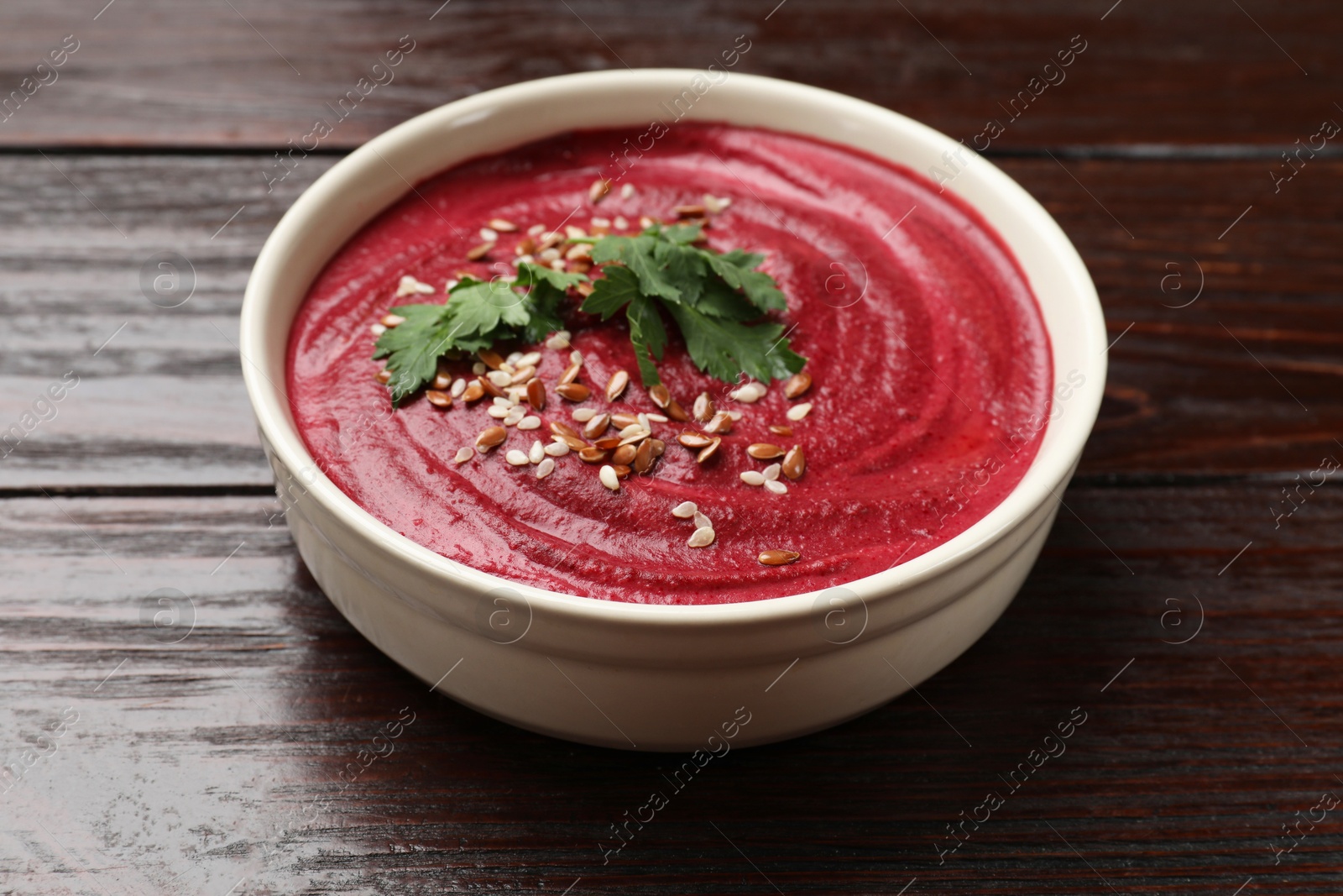 Photo of Tasty beetroot hummus, parsley and seeds in bowl on wooden table, closeup