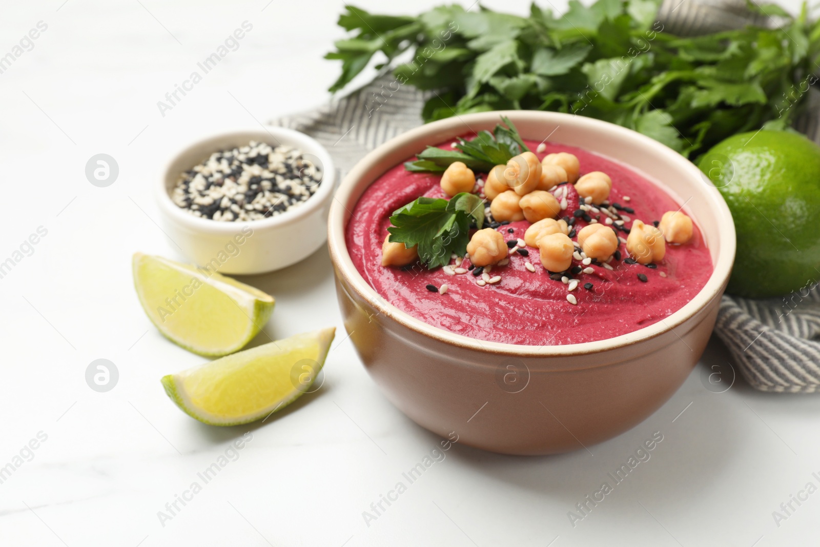 Photo of Tasty beetroot hummus in bowl and products on white marble table