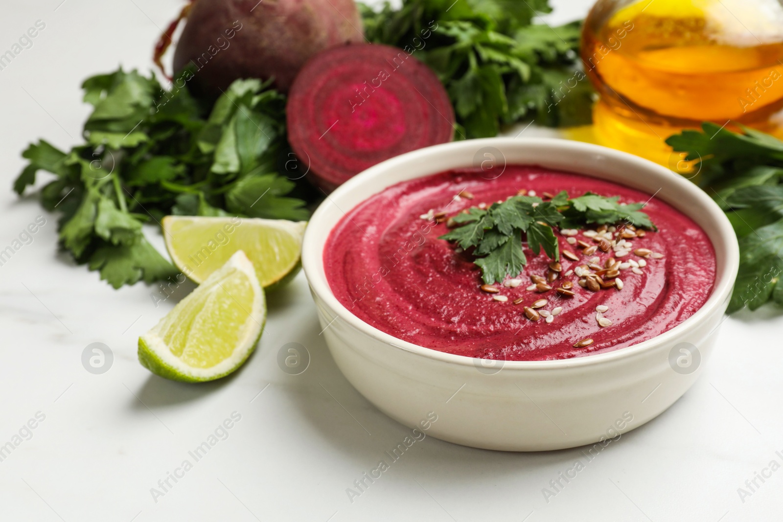 Photo of Tasty beetroot hummus in bowl and products on white marble table