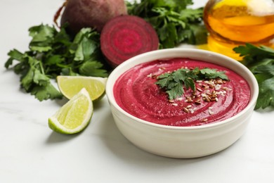 Photo of Tasty beetroot hummus in bowl and products on white marble table