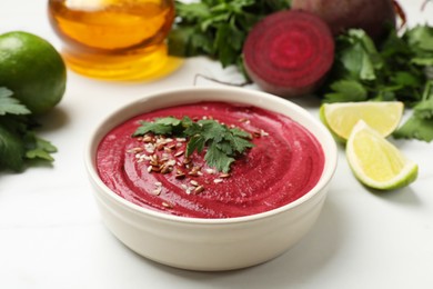 Tasty beetroot hummus in bowl and products on white marble table, closeup