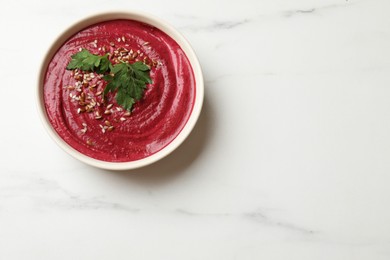 Photo of Tasty beetroot hummus, seeds and parsley in bowl on white marble table, top view. Space for text