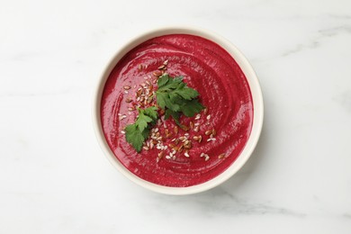 Photo of Tasty beetroot hummus, seeds and parsley in bowl on white marble table, top view