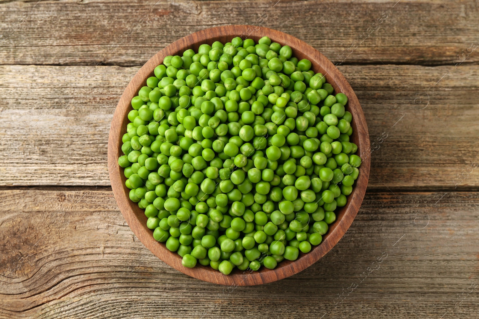 Photo of Fresh green peas in bowl on wooden table, top view